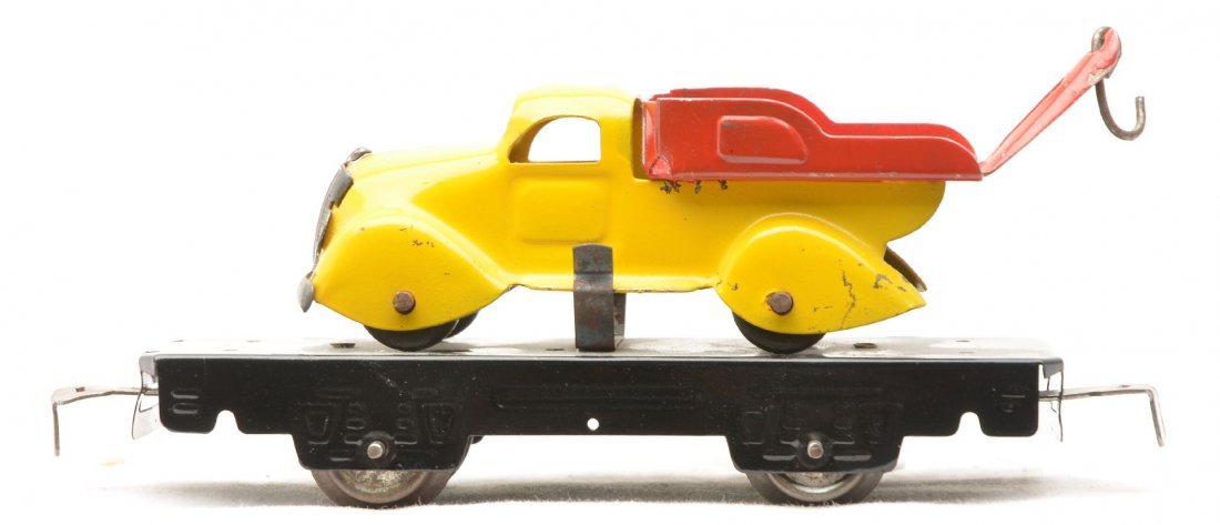 Marx 562 Black Flatcar w/Pastel Yellow Tow Truck: Marx four wheel 562 black flatcar with a pastel yellow tow truck that has a red bed. The inside of the red bed has paint touchup. Flat and truck are C6.