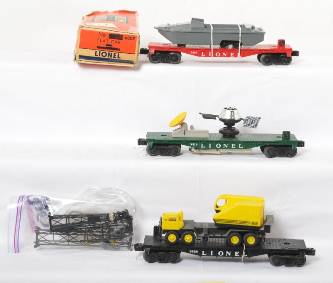 3519, 6807, and 6828 freight cars w/loads, one OB: Postwar Lionel O gauge freight cars with one box. 3519 satellite launching car, 6807 flatcar with amphibious military vehicle, and 6828 flatcar with P&H truck crane. Loads are originals, crane has a b