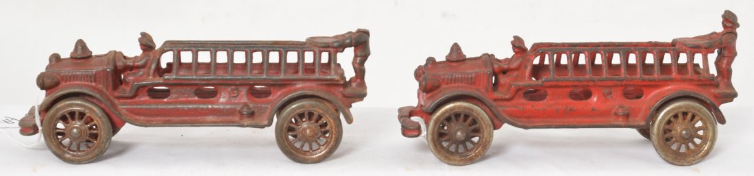 Two cast iron Fire Dept. ladder trucks: Two cast iron Fire Dept. ladder trucks with drivers in rear. Trucks have cast wheels. One is missing the rear driverÍs head. Trucks appear to be in original paint. Trucks measure approximately 7-5/8 