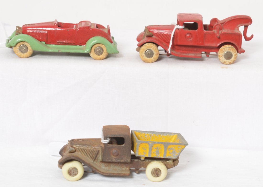 Cast iron, 2- trucks, 1- car, piano wire removable: Unmarked, casting numbers on inside, cast iron with removable piano wire and axles. Convertible coupe with rumble seat and tow truck are repainted with original tires. Dump truck appears to be origina
