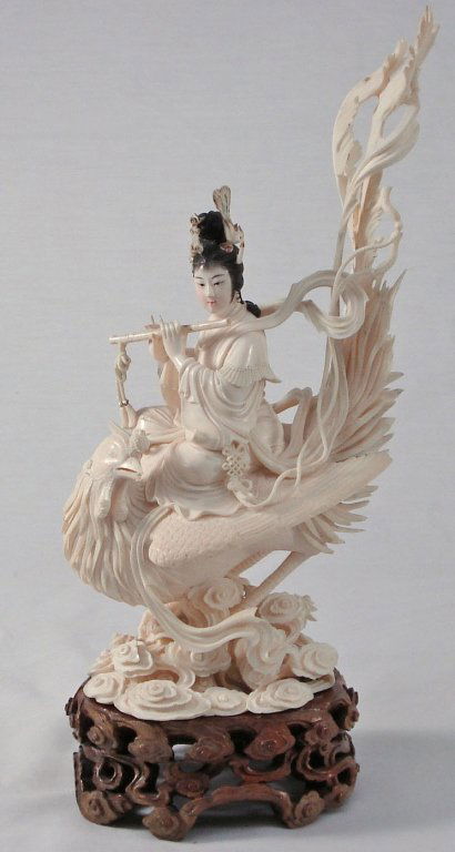 Chinese Carved Ivory Woman on Phoenix: Circa 1910 Intricately Carved Ivory Figurine of Woman in garb of flowing robes playing a muscial instrument, hair adorned with phoenix ornaments, sitting on large Phoenix on wooden base. China. Height
