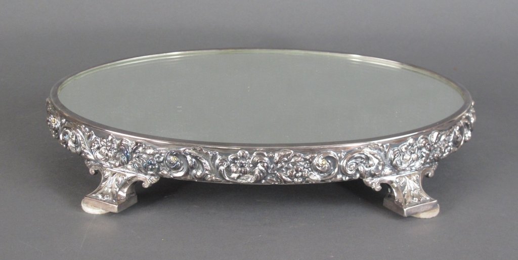 Antique Reed & Barton Silverplate Plateau Mirror: Reed & Barton Plateau Mirror, late 19th C to early 20th C, plate over bronze, oval form, decorated with a band of scroll and floral motif, raised on block feet, wood mirror base, marked "Reed & Barton