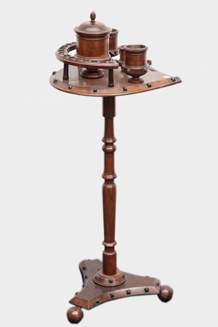 A pipe smoking table: England, early 20th centuryWood with dark patina Elegant and functional accessory for pipe smokers.Raised on a triangular base, the tall stem supports a horseshoe-shaped top, on which various recipien