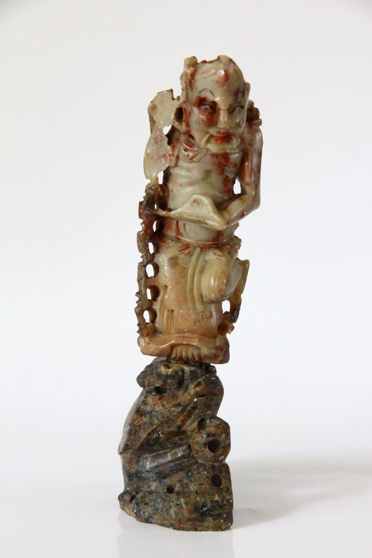 Chinese Figure Holding an Ingot: An undated detailed carved soapstone man figure standing with one leg over a dragon head and the other flexed back. Traces of paint along his mouth, eyes and eye brows. H: 6inc. (15cm). Adquired at re