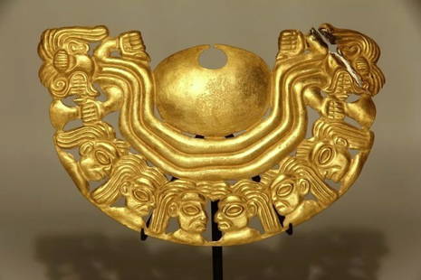 Pre Columbian Moche Gold Nose Ornament: Ancient Peru, 100-700 AD. A choice Moche tumbaga gold nose ornament with anthropomorphic heads, the flaking figures connected by three curved channels, both figures holding a tumi each. Height: 8.5 cm