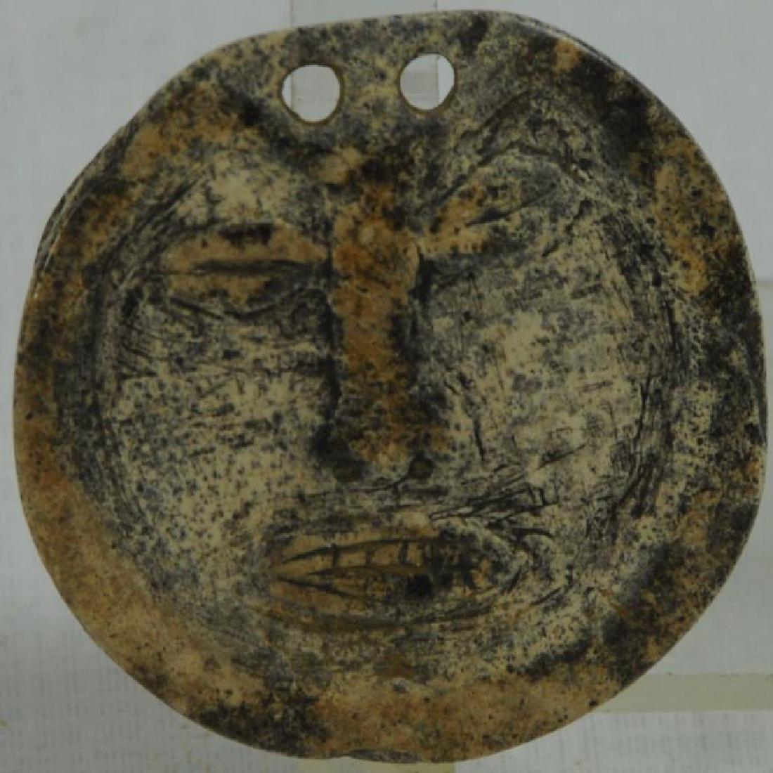 EXTREMELY RARE CULT "DEATH MASK" GORGET CARVED IN: RELIEF FROM A PIECE OF HUMAN SKULL, 1 1/2" D; 2 HOLES FOR SUSPENSION AT TOP OF FACE, PLUS INCISED RIM (FOR EAR PLUG OR LIP PLUG?). THIS IS OF THE MISSISSIPPIAN CULTURE FOUND FROM MIDDEN IN HOUSTON CO.