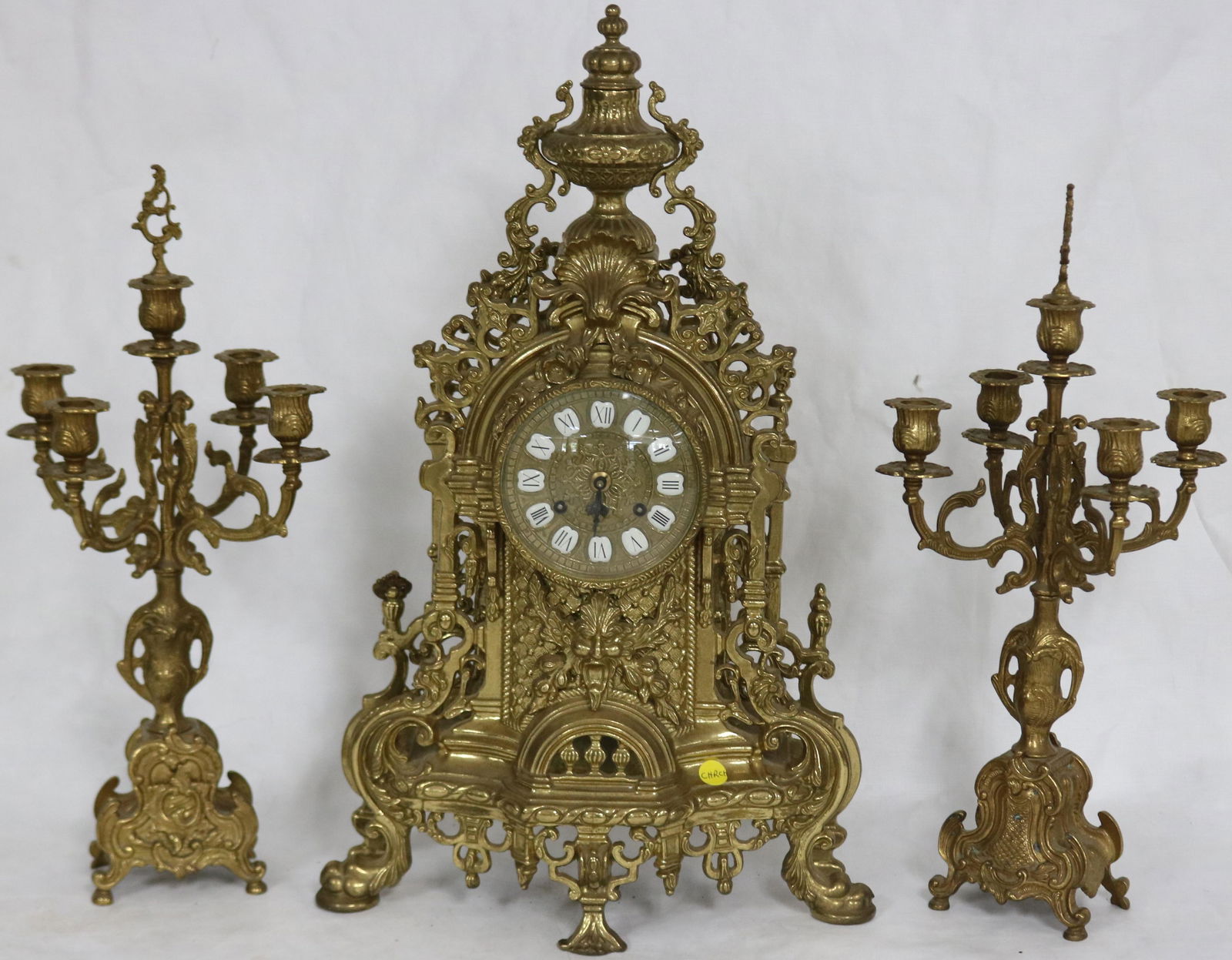 ORNATE BRASS 3 PC. CLOCK SET TO INCLUDE CLOCK: WITH ENAMELED NUMBERS, MINUTE HAND MISSING, SPRING GOOD, UNKNOWN WORKING CONDITION, 24" H, 14" W, 6 1/4" DEEP WITH PAIR OF MATCHING 5 SOCKLE CANDELABRAS, 9 1/2" H, 7 1/2" X 9" W