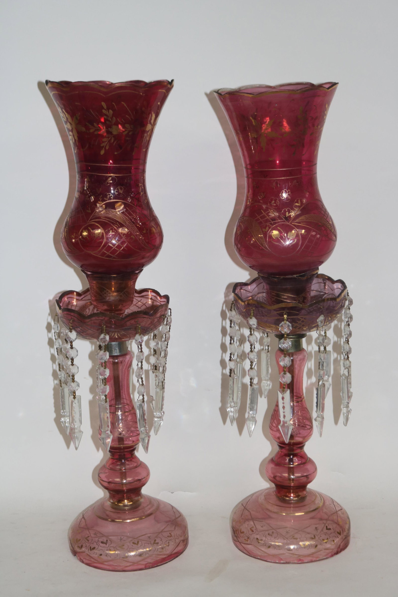 PAIR OF GILT AND FLASHED MANTEL LUSTER LAMPS: CRANBERRY COLOR, ONE SHOWS CHIP ON CANDLE CUP, 26 1/2" H. 6 1/4" DIA AT TOP.