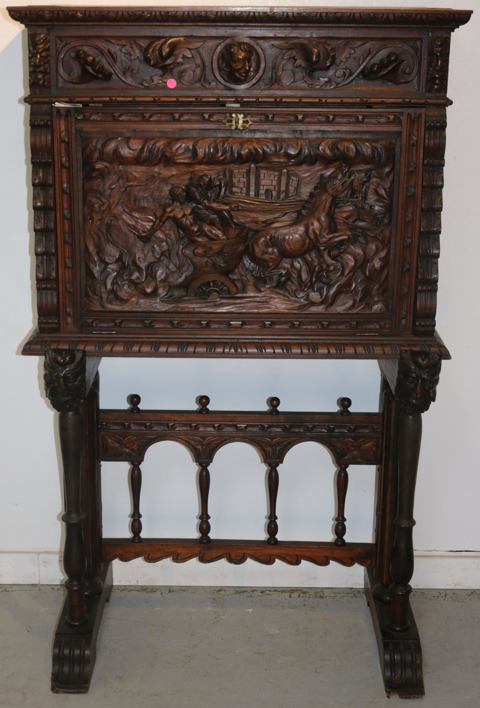 ORNATELY CARVED DESK ON STAND, FALL FRONT, CARVED: WITH CHARIOT & HEAD, CARVED LID SUPPORTS, BASE SHOWS NICK TO FOOT, ORIGINAL FINISH, 20TH C. 60 1/2" H, 37" W, 20 1/2" D