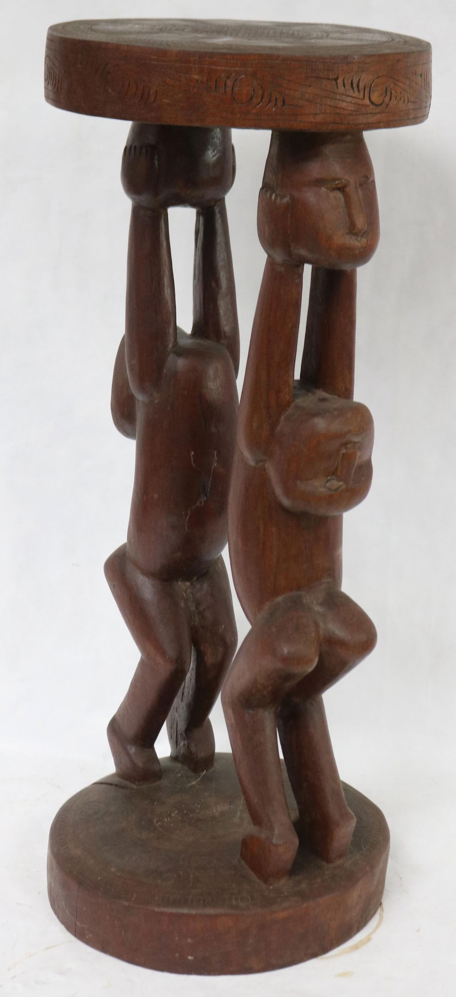 TRIBAL CARVED HARDWOOD STOOL WITH HUMAN EFFIGY: SUPPORTS HOLDING HEADS SUPPORTS, GEOMETRIC CARVED TOP, 24 1/2" H, 9 1/2" DIA.