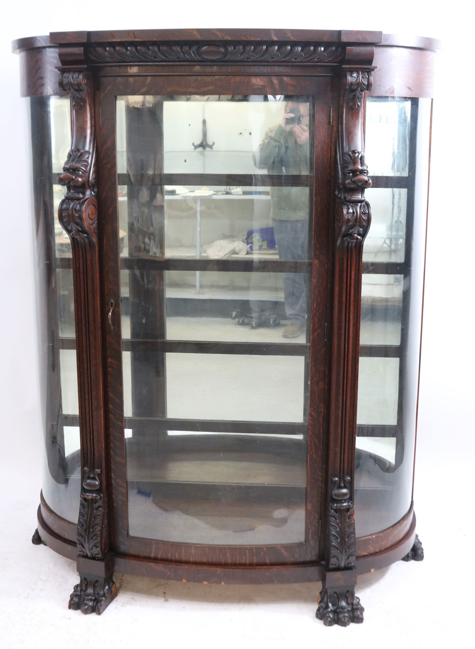 LATE 19TH C. CARVED OAK CURVED GLASS CHINA: CABINET, CARVED TOP, WINGED GRIFFIN FRONT, REEDED COLUMNS, CARVED LARGE CLAW FEET, 1 FOOT MISSING PIECE, OLD DARK FINISH, MIRROR BACK, GLASS SHELVES, 66 1/2" H, 64" W, 21" D, MINOR VENEER LOSS AT BASE