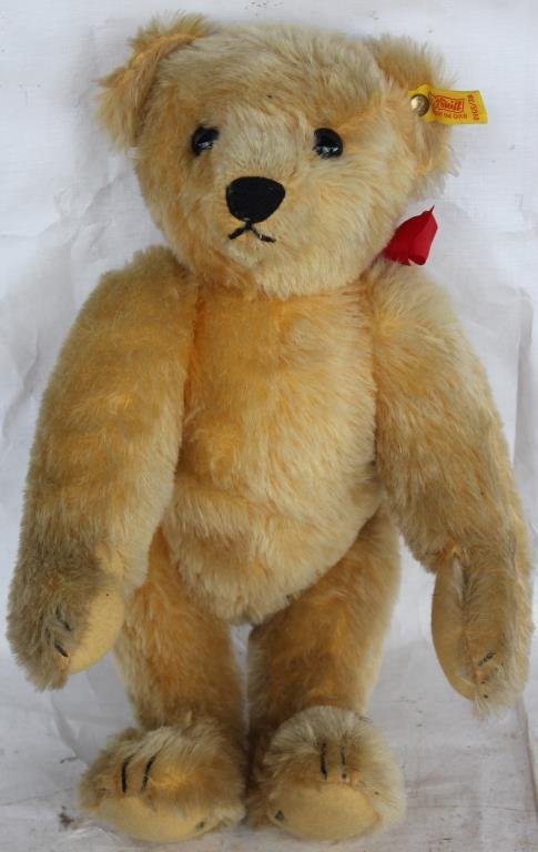 STEIFF 38 GOLDEN BEAR, 0165, NO BOX AND HAS: 1 HOLE IN EACH FOOT WHERE HE WAS STUCK WITH STAND TO HOLD HIM. HAS RED RIBBON, WELL-LOVED CONDITION.