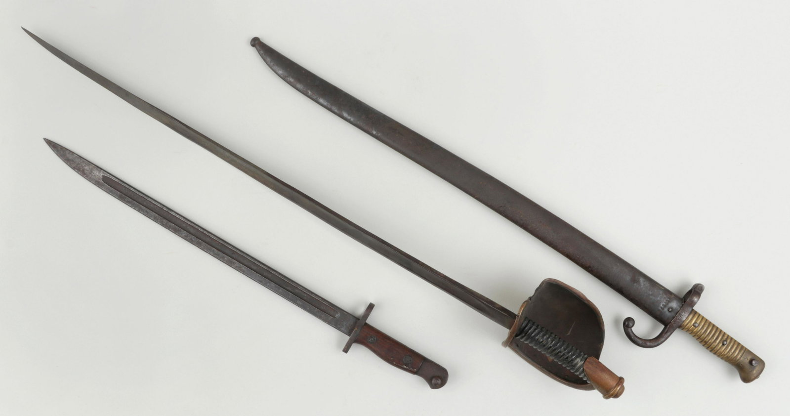 Group of (3) swords: Group of (3) swords, to include: sabre; Remington bayonet 1907 with wood handle; and bayonet with sheath. All marked. Wear from age. Longest 31-1/4''l.