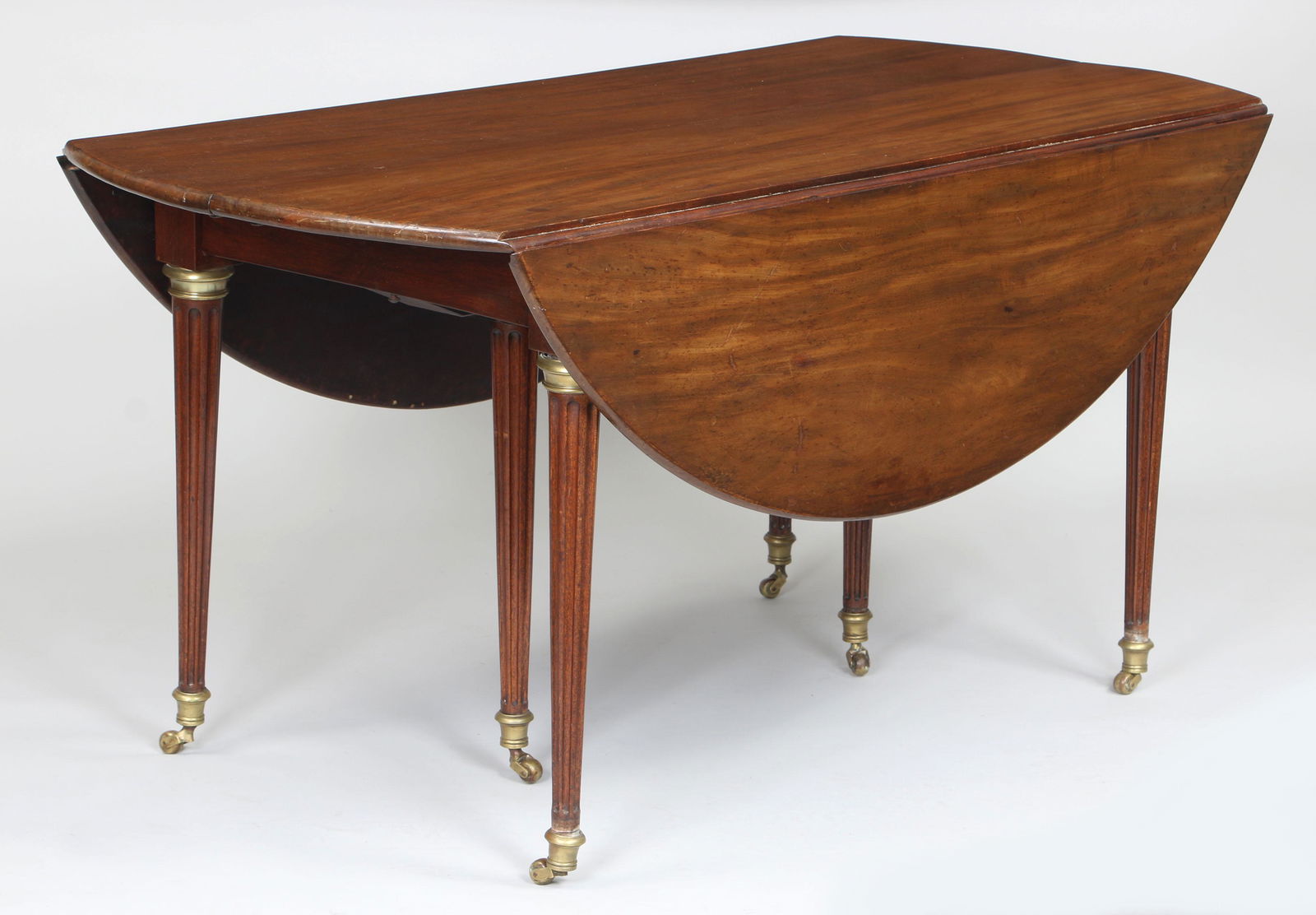 19th century French Directoire circular dining table: 19th century French Directoire circular dining table with drop ends, on six round tapering fluted legs and bronze mounts, along with two additional extension leaves. Top shows wear and refinishing, re