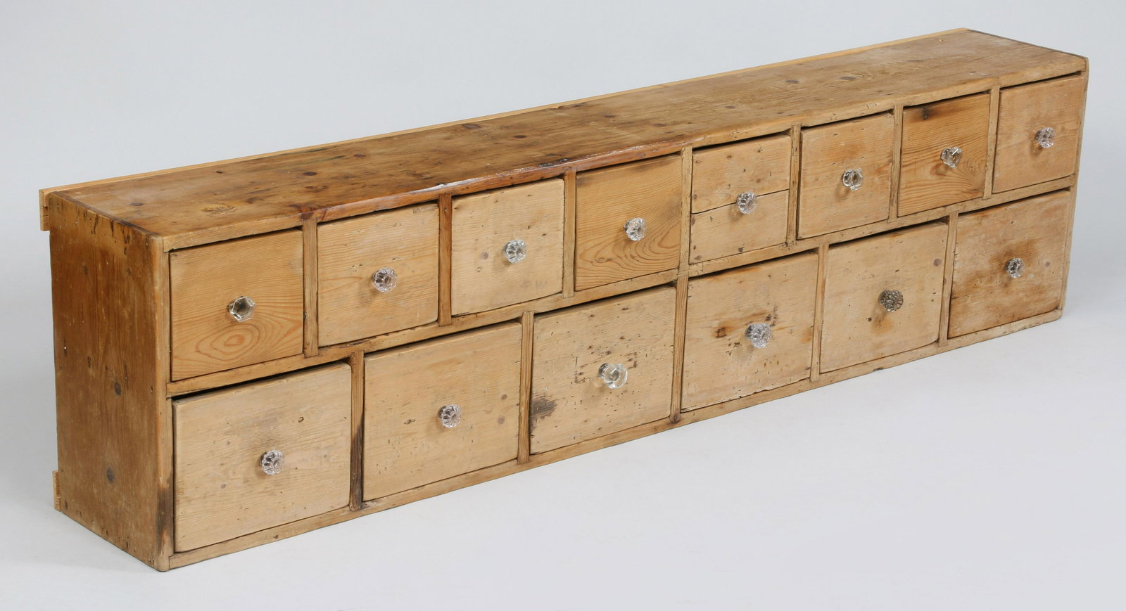 Fourteen drawer pine apothecary: Fourteen drawer pine apothecary with assembled set of glass knobs. Some drawers replaced. 18''h, 71''w, 10-1/2''w.