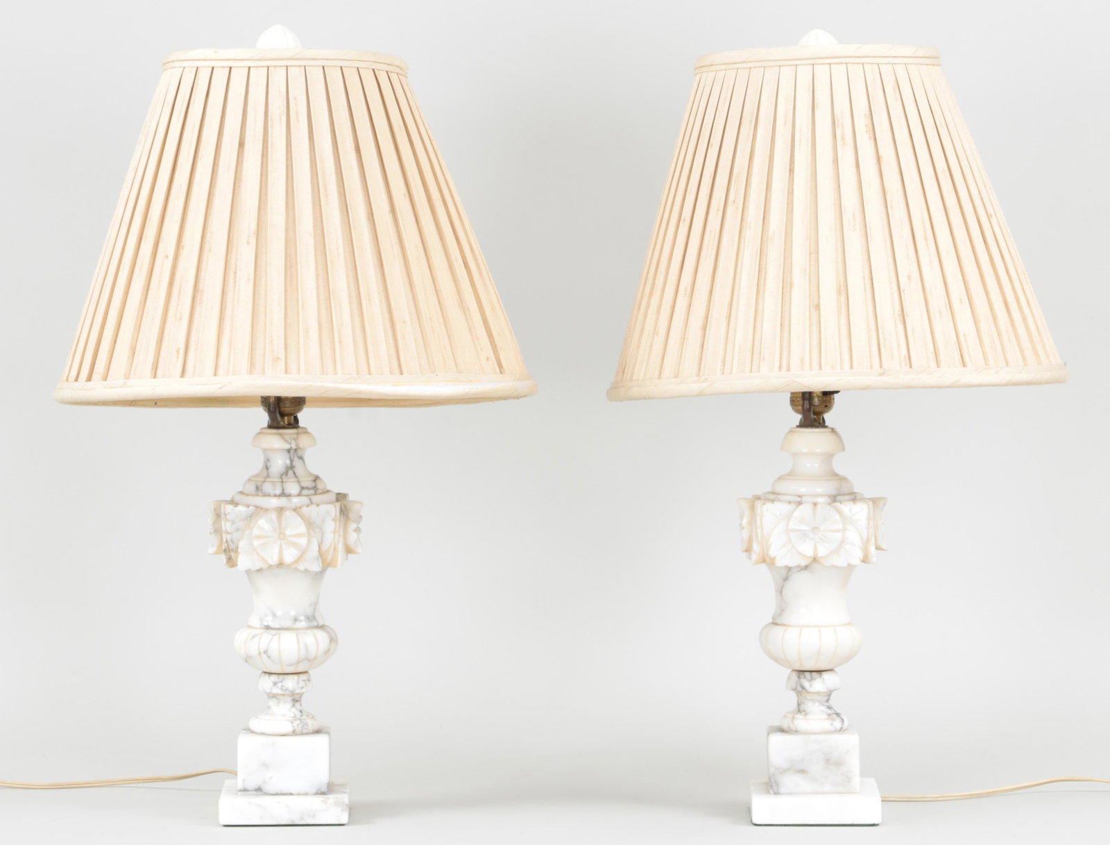 Pair of alabaster urn-form lamps: Pair of alabaster urn-form lamps with carved finials and rosette medallions, raised on stepped square bases. Chips, one base with hairline. 12''h.