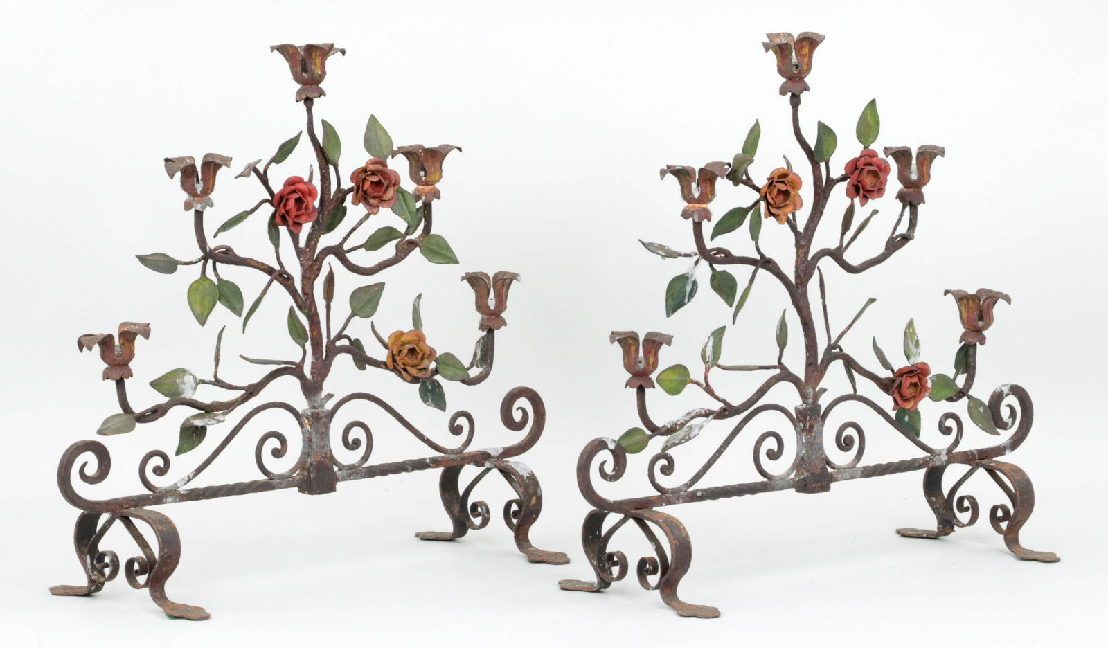 Pair polychrome painted wrought iron candelabras: Pair of Italian polychrome painted wrought iron five-light candelabras with floral and foliate decoration, raised on scroll legs. Paint loss and wax residue. 18-1/4''h, 20-1/4''w, 7-3/4''d.