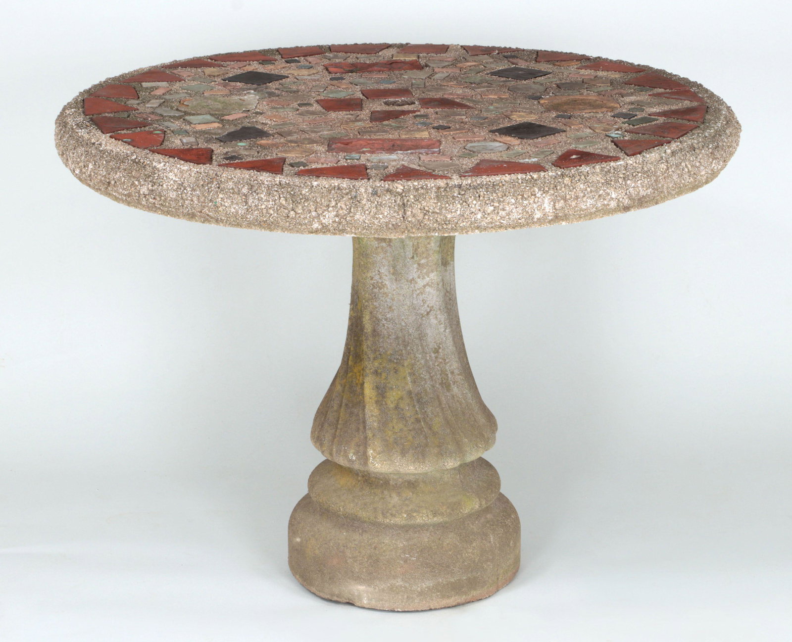 Mosaic-top cast stone garden table: Mosaic-top cast stone garden table with inset tile and brick. Weathered, tile loss and fill. 30''h, 39''dia.
