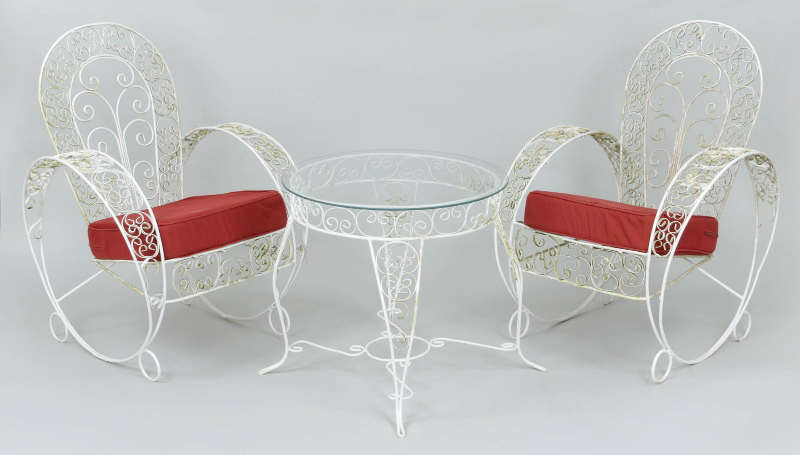 Three-piece iron patio set: Three-piece iron patio set to include a pair of armchairs with cushions and round glass top cocktail table. Some scrollwork misshapen, stains to cushions. Armchairs 36''h, 26-1/4''w, 24''d. Table 22-3