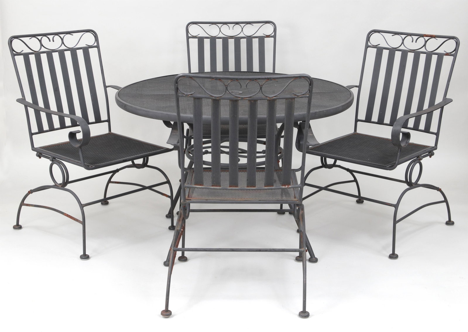 Five piece wrought iron patio set: Five piece wrought iron patio set, to include: round table with mesh top; (4) rocking arm chairs with scrolled crestrail, mesh seats, and spring rockers. Some paint loss, wear to springs. Table 28''h,