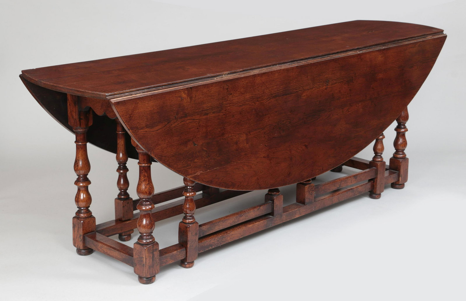 Large oak gateleg dining table: Large English oak drop-leaf gateleg dining table, having oval top set on baluster-turned legs joined by stretchers, on bun feet. 30''h, 84''w, 22''d (closed), 60-1/4''d (open).