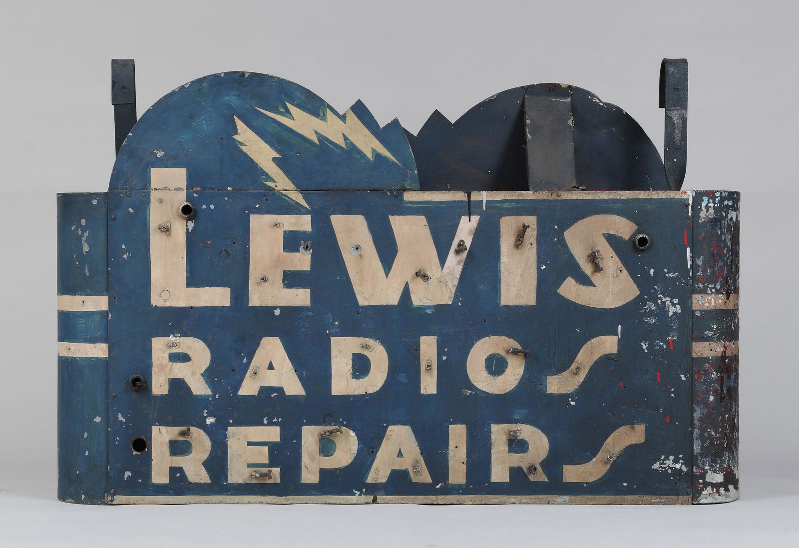 Double sided hanging sign: ''Lewis Radios Repairs'' double sided hanging sign, with painted letters and lightening bolt, neon tube fittings. Paint loss, lacking neon tubing, top supports and cover damaged. 40-1/2''h, 62-3/4''w,