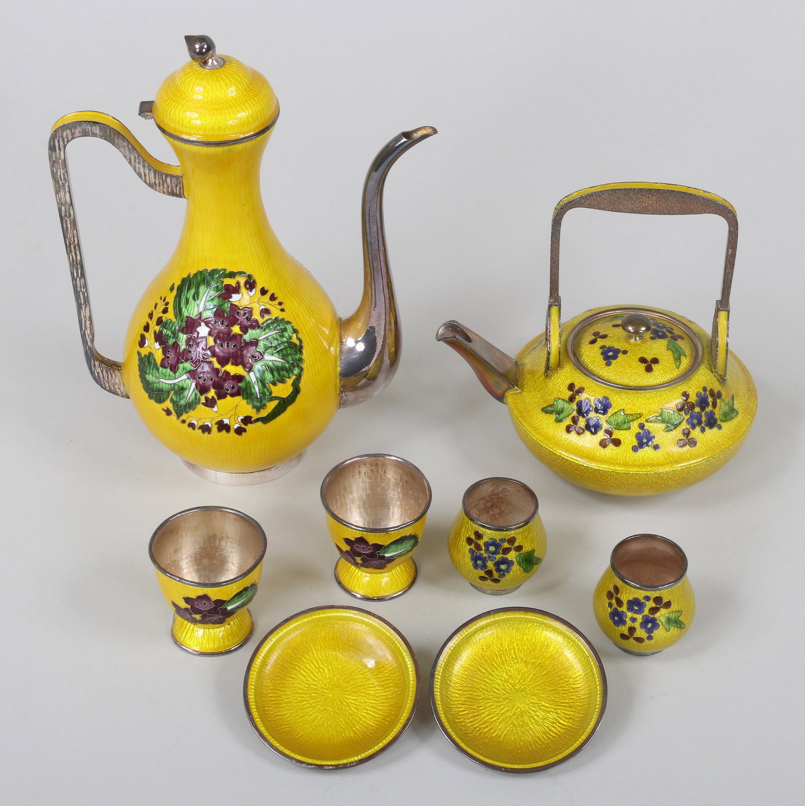 Asian enamel silver tea services: Group of (2) Asian cloisonne enamel silver tea services with floral patterns, to include: Large tea pot and (2) matching cups, (enamel wear, hinge break and dent to coffee lid); and small teapot with