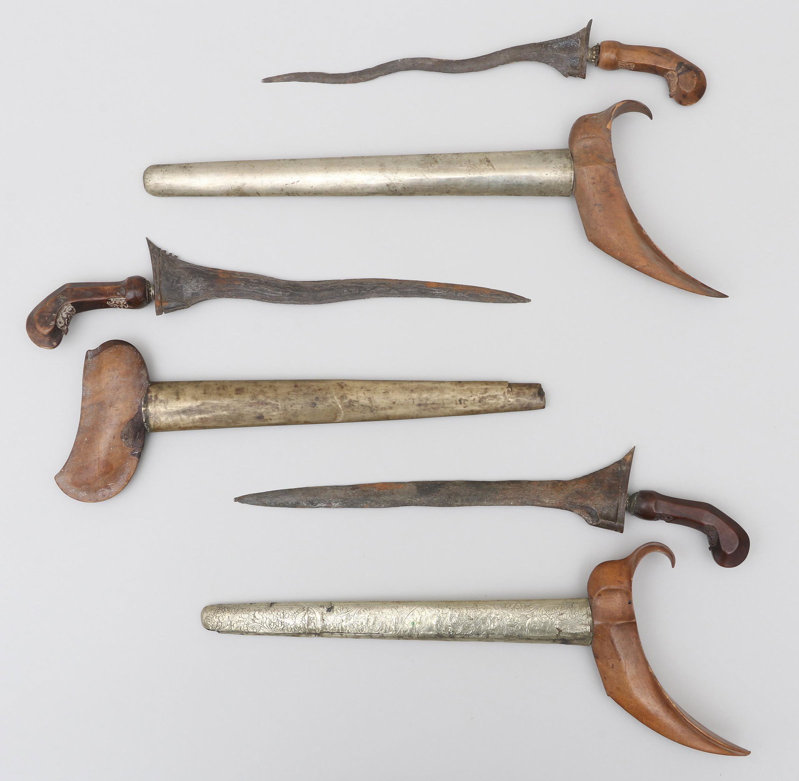 Kris daggers: Group of (3) kris daggers with forged wavy blades, carved wood handles, and metal wrapped scabbards, 19th century. Wear, some chips and losses. Provenance: Estate of William Kranker, collector and dea
