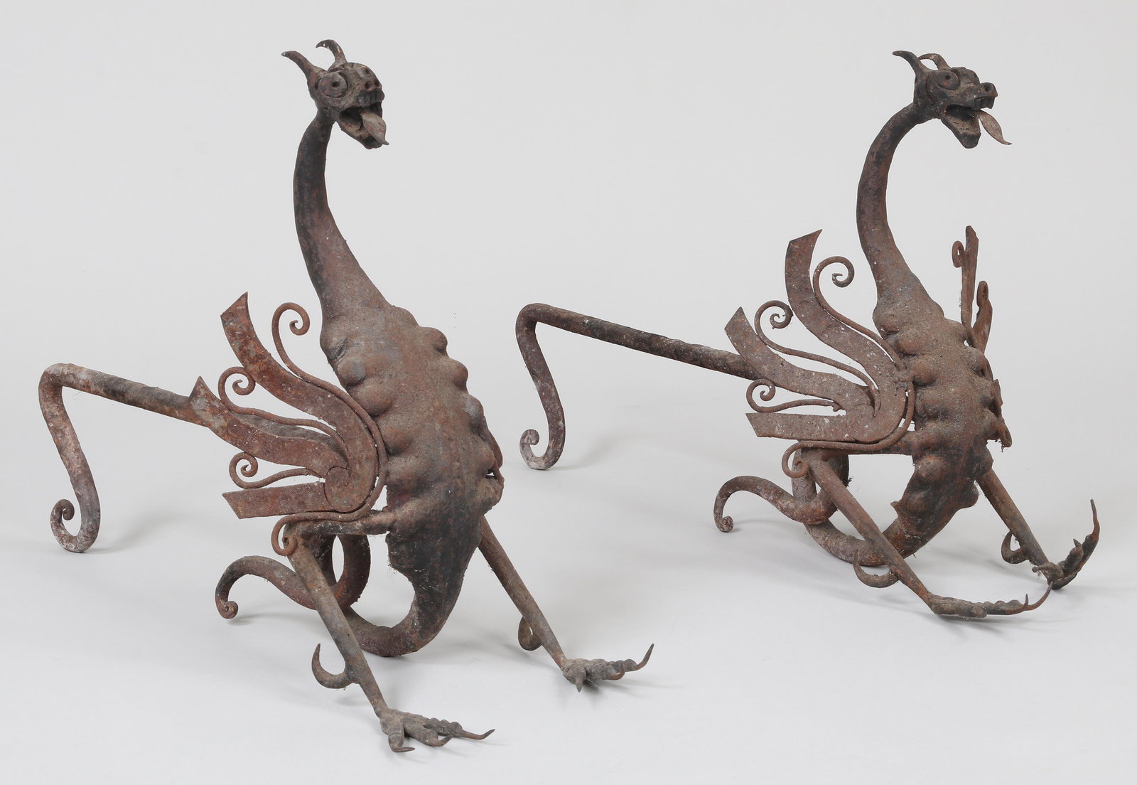 Wrought iron dragon andirons: Pair of hand wrought iron dragon andirons. Some misshaping, one wing with detached spot weld. 14-1/2''h, 21-3/4''l, 9''w.