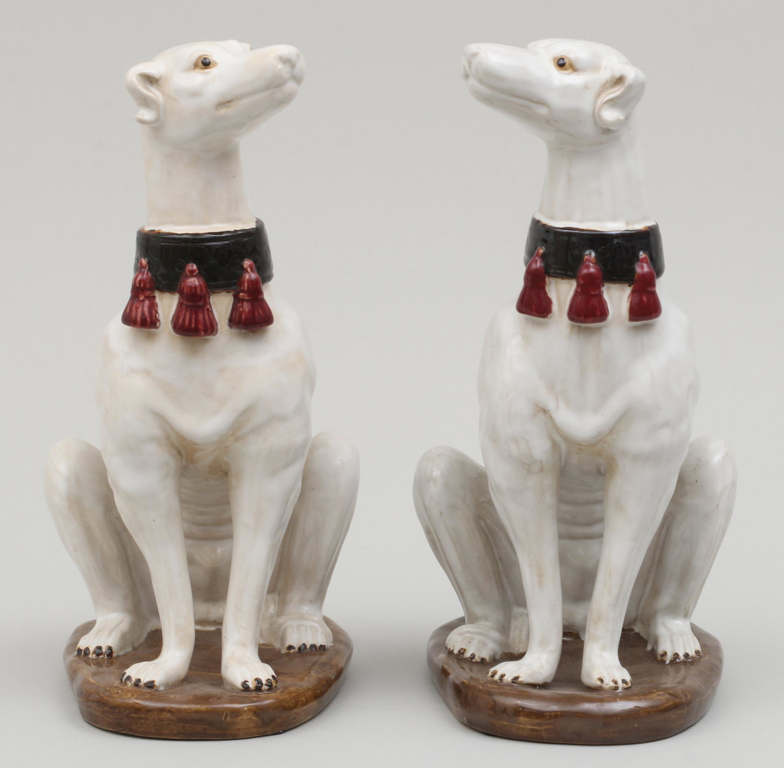 Pair of glazed ceramic whippets: Pair of glazed ceramic whippets with tassel collars, seated on oval bases. Craquelure to collar of one, wear from use. 14''h.