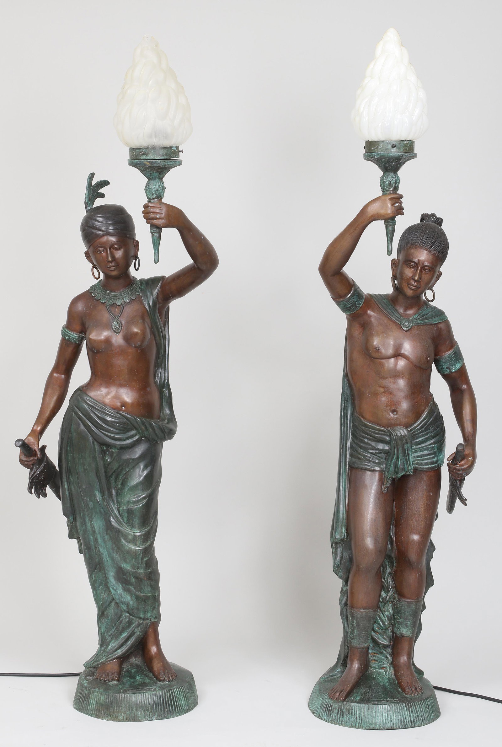 Pair of large figural bronze torchieres: Pair of large figural bronze torchieres, depicting tribal figures, late 20th century, bases with plaque marked ''Leonardo Rossi'', electrified. One replaced hoop earring, one shade and socket damaged,