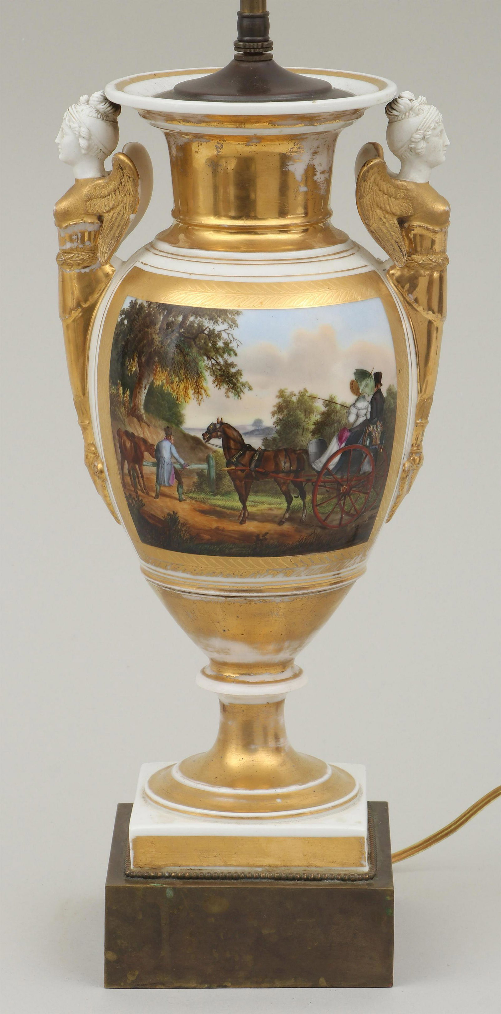 Neoclassical-style porcelain urn-form table lamp: Neoclassical-style porcelain urn-form table lamp, having a hand-painted scene depicting a carriage ride, two handles in the form of winged maidens, and gilt decoration, electrified. Losses to gilt, ha