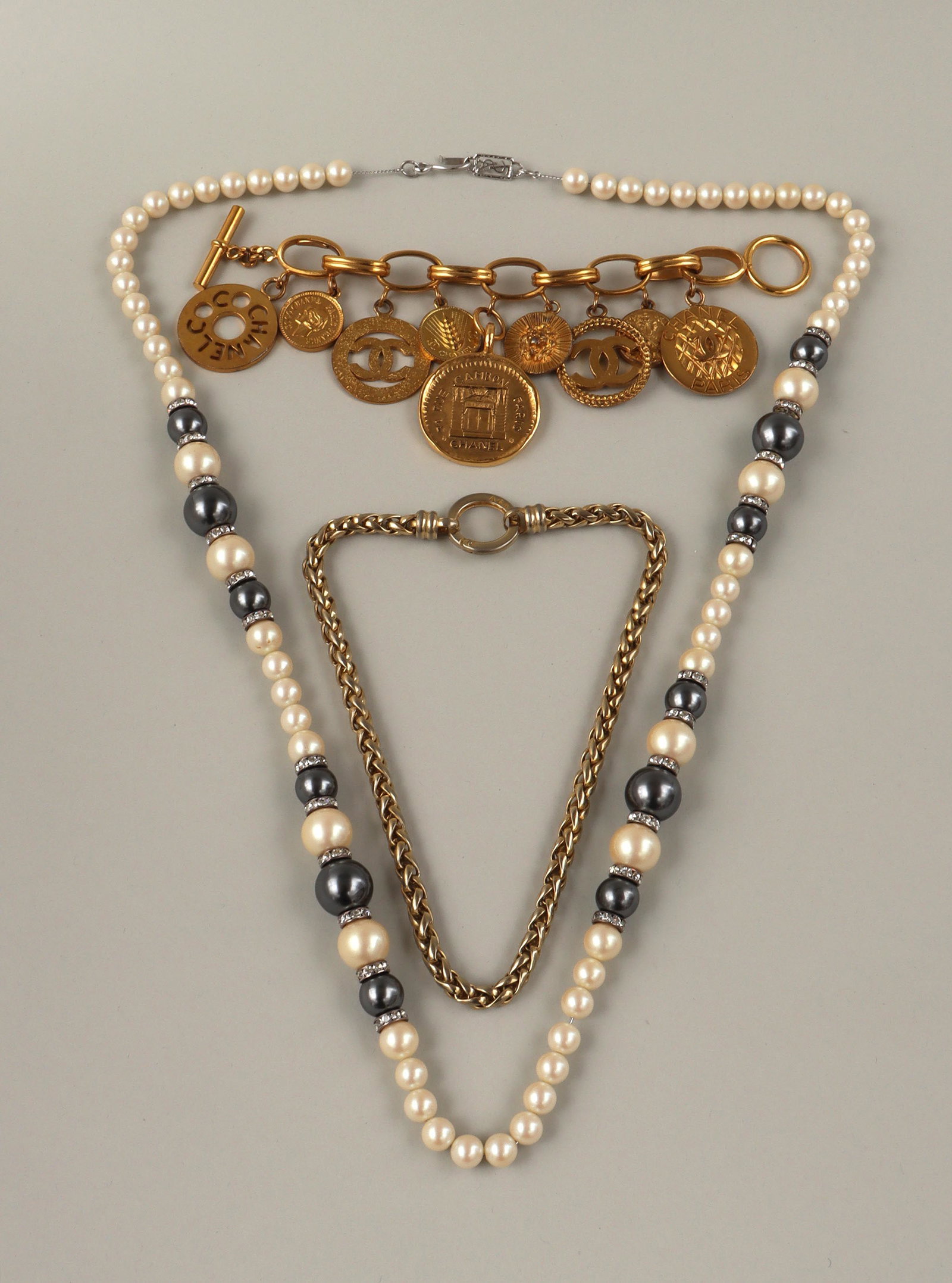 Chanel,YSL and Agatha: Group of (3) designer costume jewelry, to include: Chanel gold-plated charm bracelet, with (9) oversized Chanel symbol disk charms; Yves Saint Laurent long pearl necklace, string of artificial pearls 
