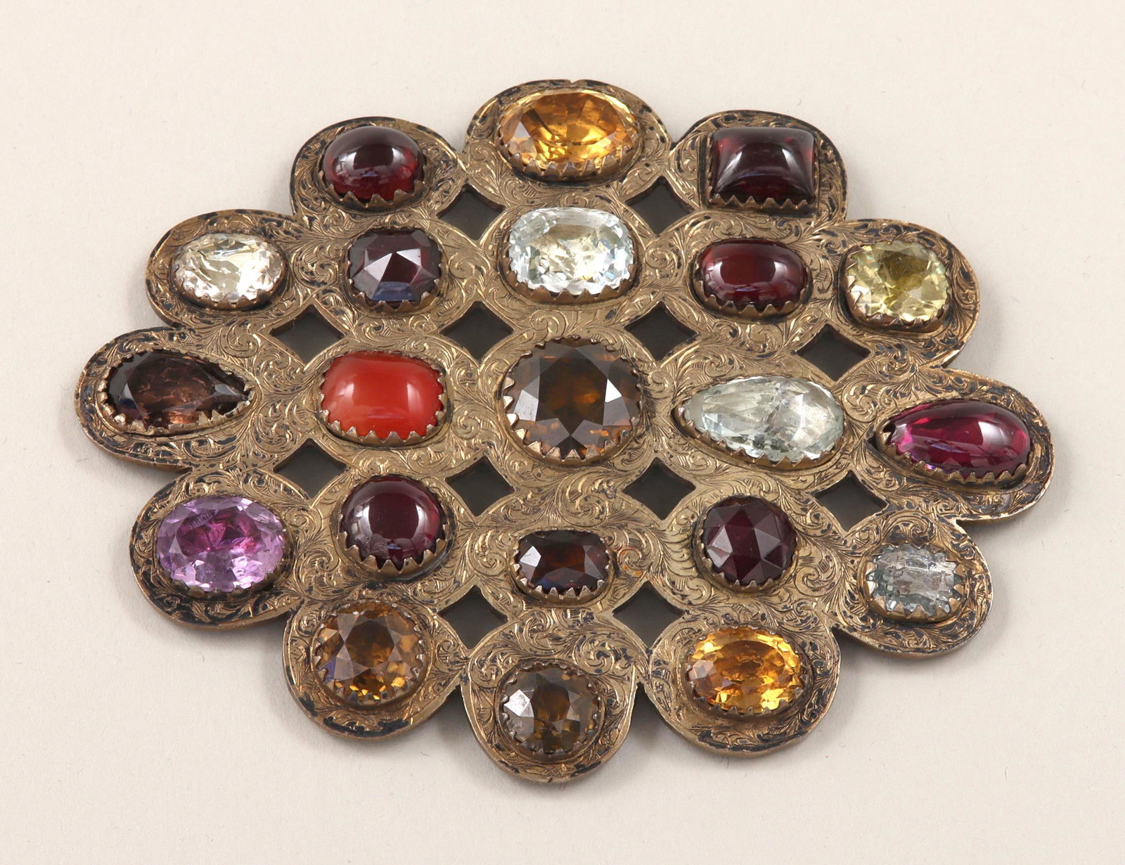 Gilt silver belt buckle: Gilt silver belt buckle with semi-precious and glass stones, having pierced and engraved scrolled design with (21) inlaid stones, comprising (7) red garnet, (4) semi-precious colorless stones, (2) ova