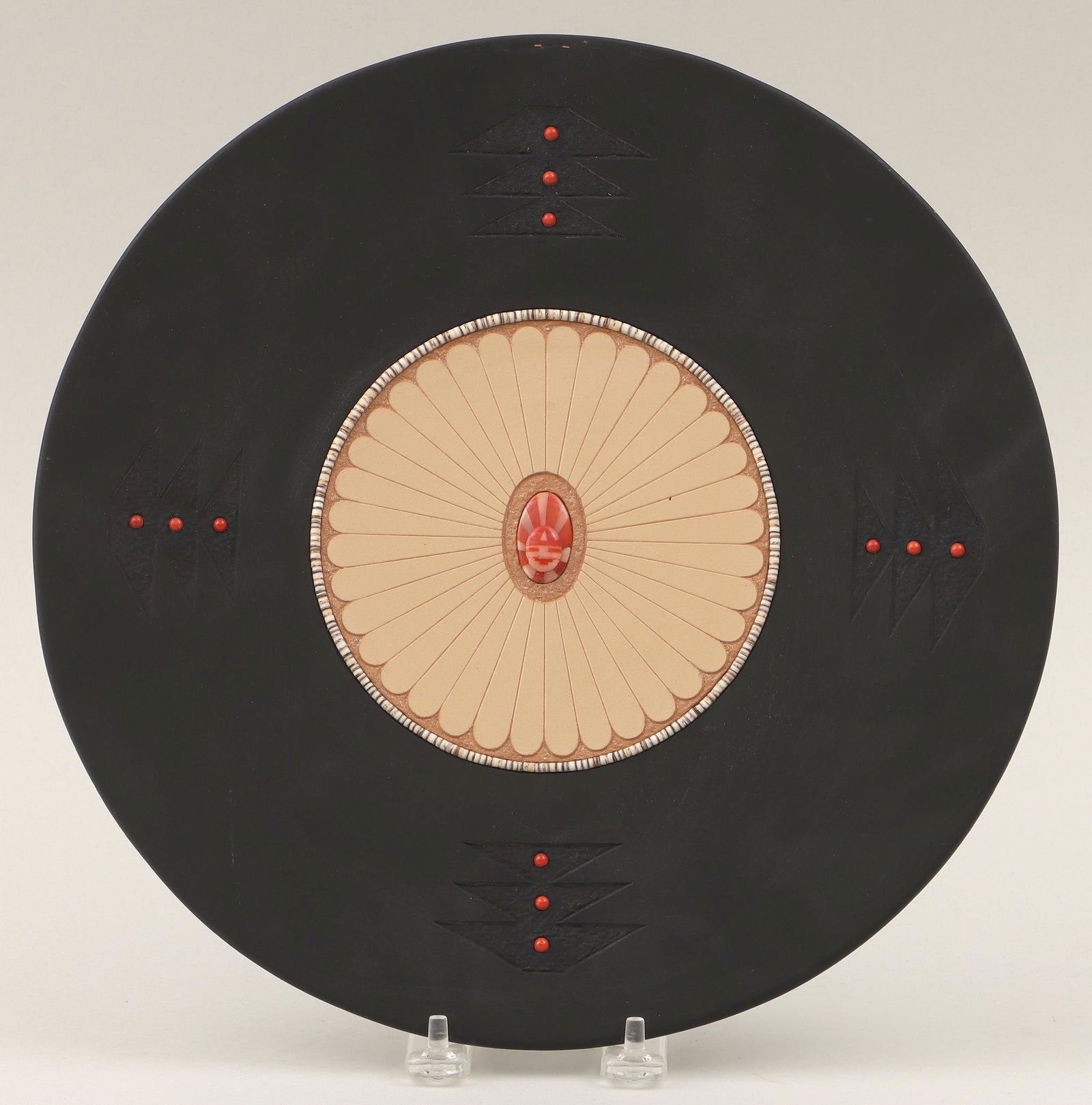 JOHN GONZALES: JOHN GONZALES (San Ildefonso Pueblo, b. 1955), pottery plate, having painted black edge with (9) coral cabochons and central circle with pieced coral mask, micaceous clay and heishi bead border, 1996,