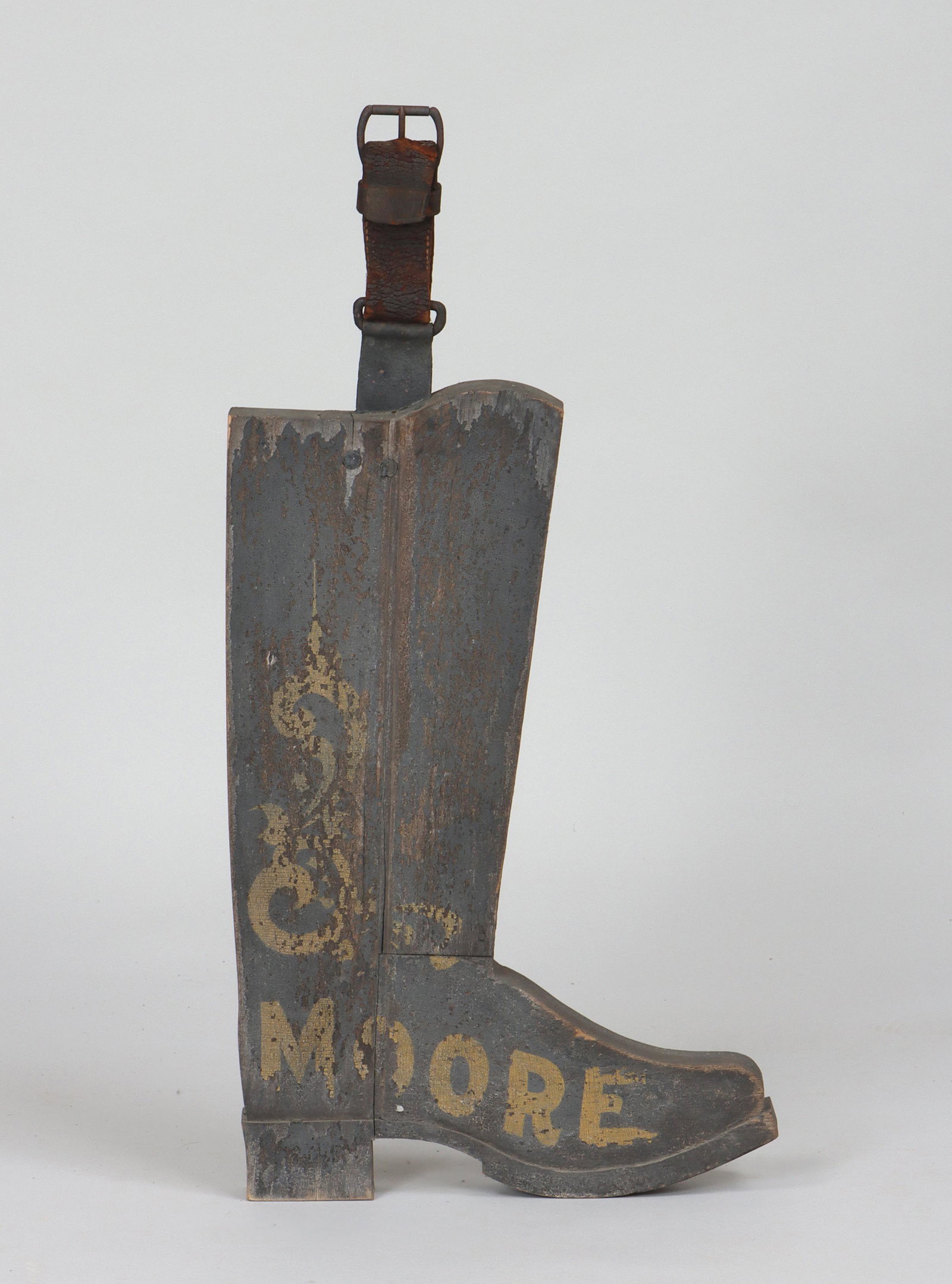 Carved and sand-painted bootmaker's trade sign: Carved and sand-painted bootmaker's trade sign, with ''Moore'' lettering, and leather hanging strap. Paint flaking, wear from use. 22-3/4''h, 14-1/2''w, 1-3/4''d. Provenance: Estate of Joseph ''Jay'' 