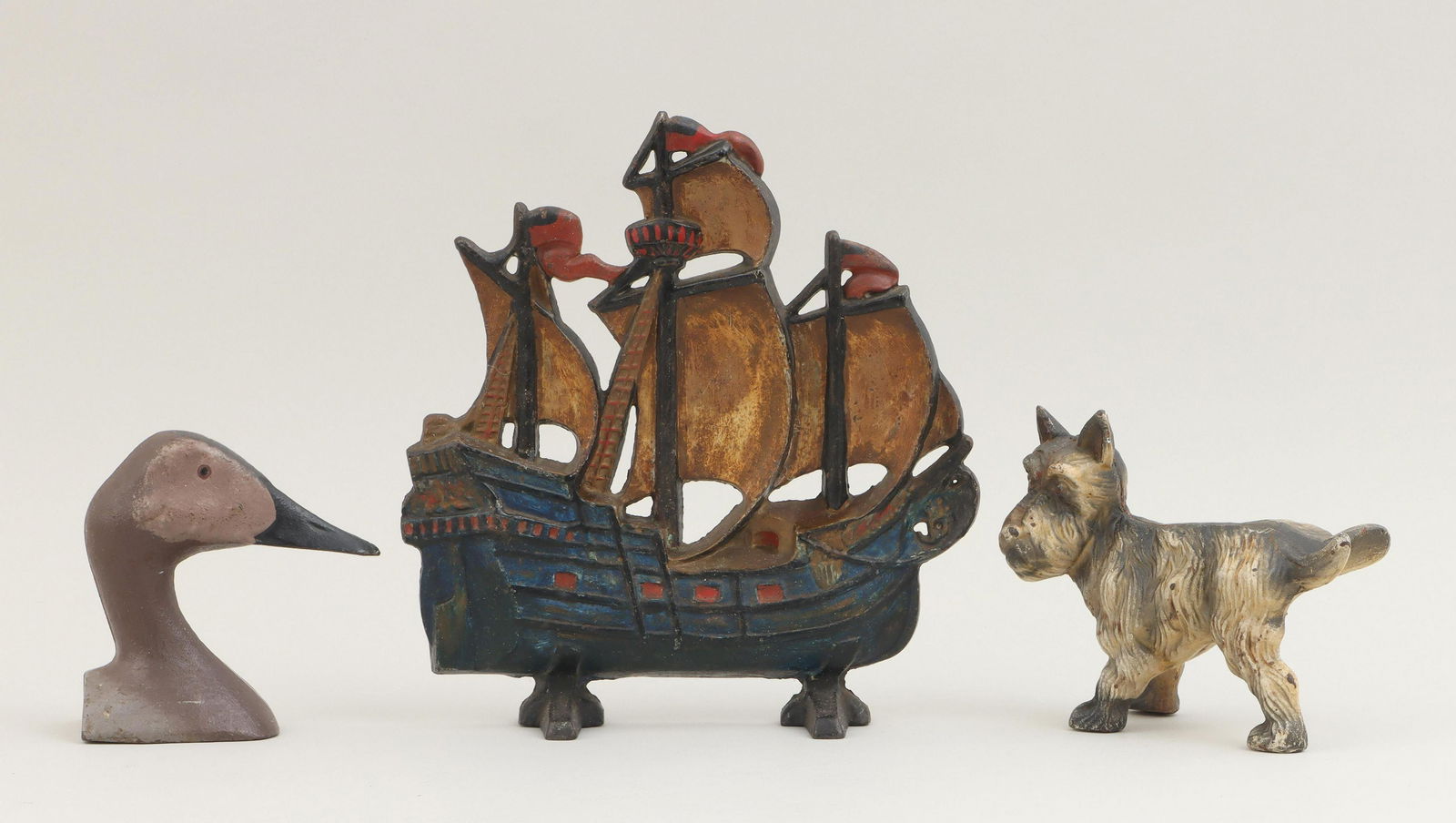 Group of (3) cast iron doorstops: Group of (3) cast iron doorstops, to include: three-masted ship; duck head; and Scottish terrier with lifted leg. Paint losses and minor oxidation. Ship 12''h, 11-1/2''w, 3''d. Provenance: Estate of J