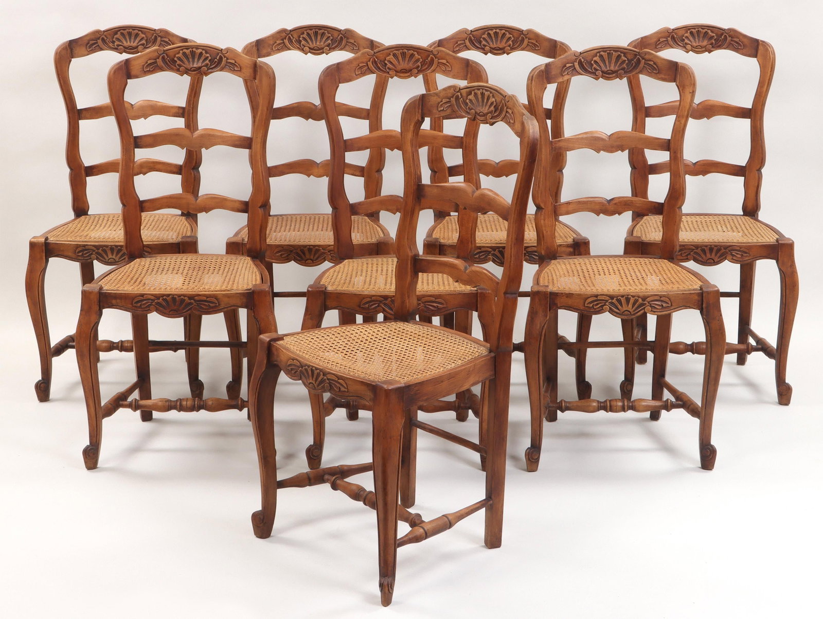 (8) French Provincial style chairs: Set of (8) French Provincial style walnut dining chairs, having shell-carved crestrail and apron, caned seats, cabriole legs, turned stretchers and scroll-carved front feet. Minor wear from use includ