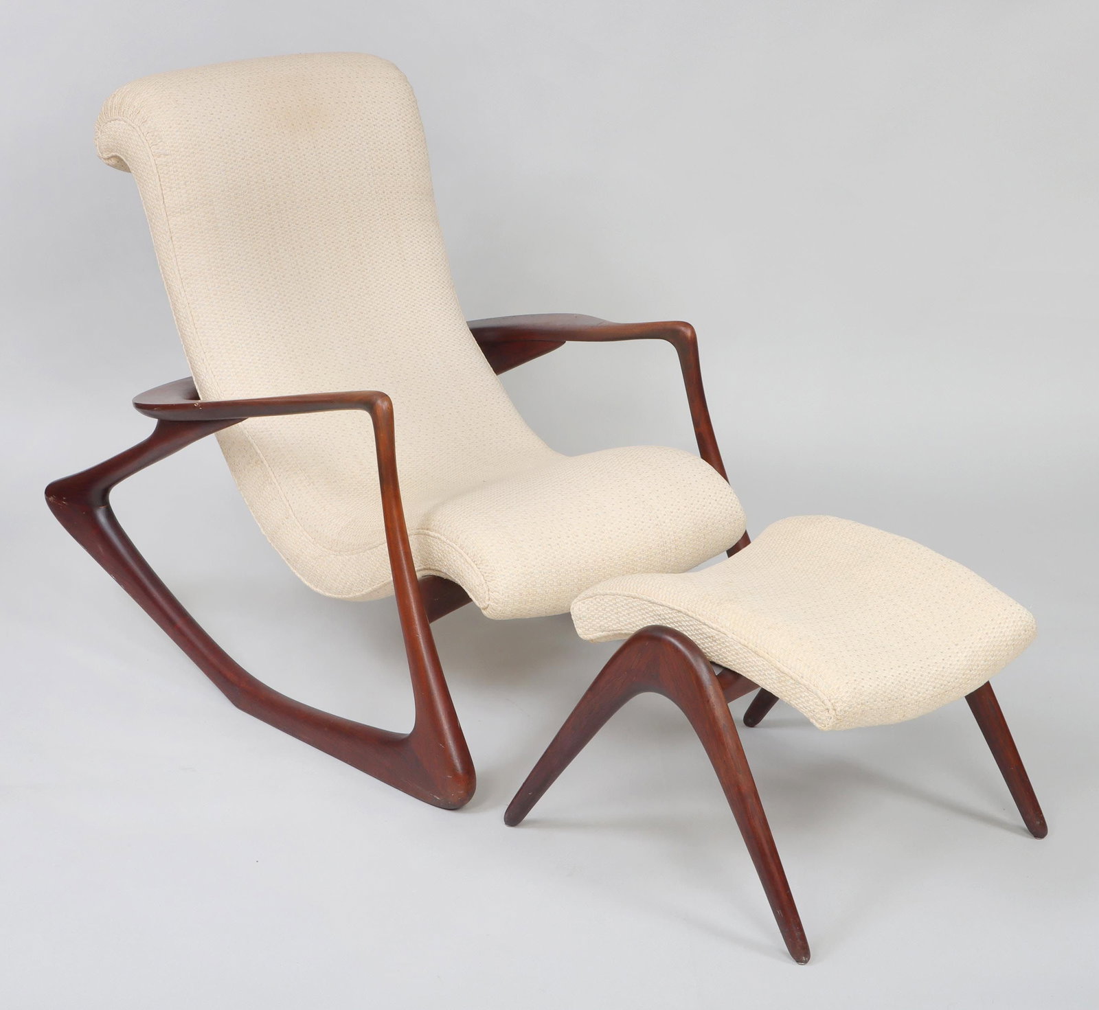 VLADIMIR KAGAN (American, 1927-2016): VLADIMIR KAGAN (American, 1927-2016), sculpted walnut two-position rocking chair and ottoman. Minor scuffs and wear from use, dent to arm, some stains to fabric. 37''h, 32-1/2''w, 44''d.
