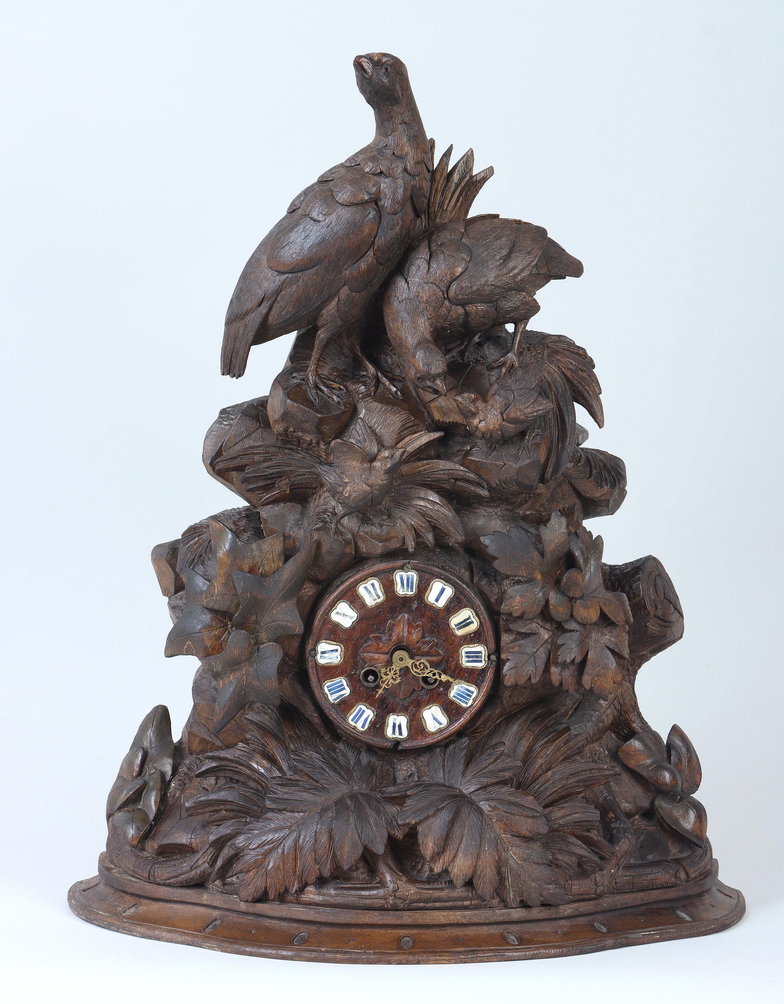 German Black Forest carved clock: German Black Forest carved wood figural clock with a family of quail surrounded by plants, having wood face with applied enamel Roman numerals and gilt scrolled foliate hands, most likely 19th century