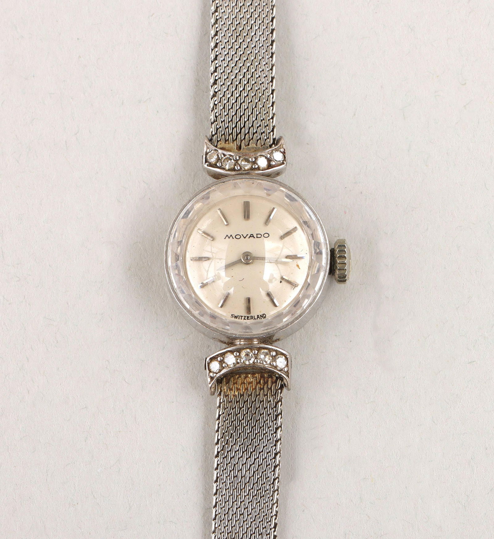 Movado 18k white gold ladies' wristwatch: Movado 18k white gold ladies' wristwatch, 17 jewels, movement no. 2287, case no. C8613, with round face flanked by (10) round-cut diamonds, set in a pair of C-curves covering the inner ends of the mes