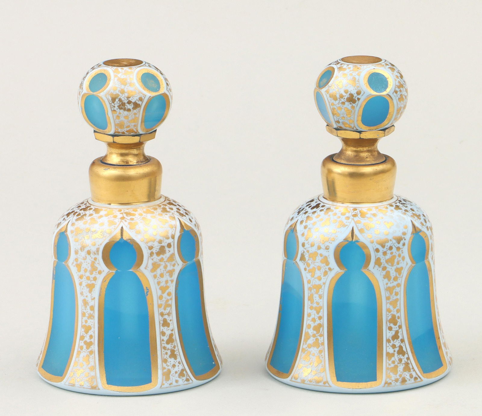 Pair of Bohemian glass overlay bottles: Pair of Bohemian glass overlay bottles with stoppers, having white-cut-to-blue sides with Moorish arches and gilt floral decoration. Chips to bottoms of stoppers, some loss to gilt decoration; one bot