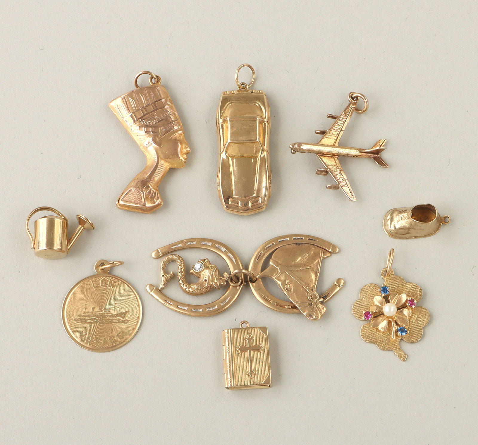 Group of (11) gold charms: Group of (11) gold charms, to include: (9) 14k charms, comprising locket in the form of a book with a cross on the front, sportscar with articulated wheels, watering can, baby shoe inscribed ''Lisa 6-