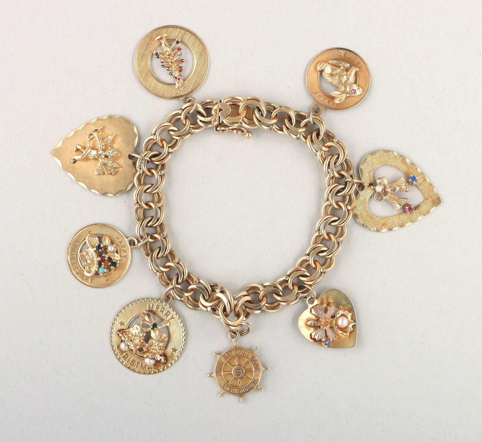 14k gold charm bracelet: 14k gold charm bracelet, having parallel chain with (8) disc charms, charms to include: ''Happy Easter'' having rabbit with ruby eye; wedding bells in a heart having semi-precious pink stone clapper, 