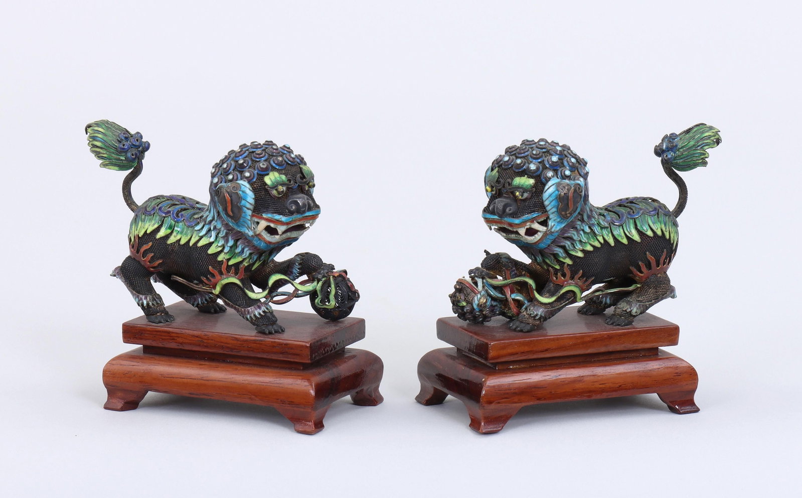 Small Chinese silver cloisonne foo dogs: Pair of small Chinese silver cloisonne foo dogs, one with sphere, the other with a smaller foo dog, on footed wood bases. A few minor losses to enamel. Each approximately 4''h, 2-1/4''w, 3-1/2''d.
