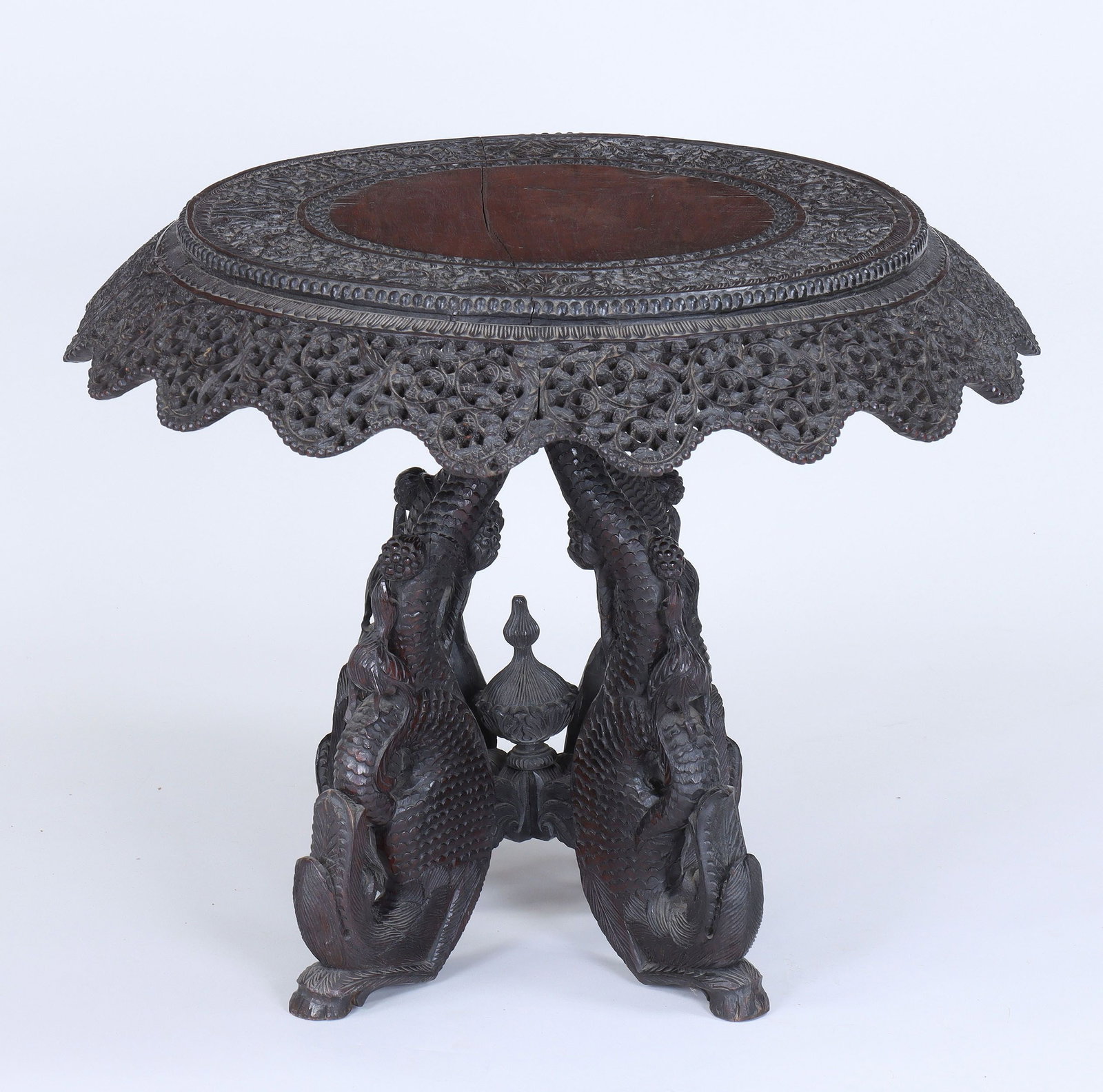 Carved and pierced Burmese table: Carved and pierced Burmese table, with foliate and landscape scenes carved in relief to round top, over quadripartite base with dragon-form legs ending in hoof feet. Splits, minor chip, wear from use.