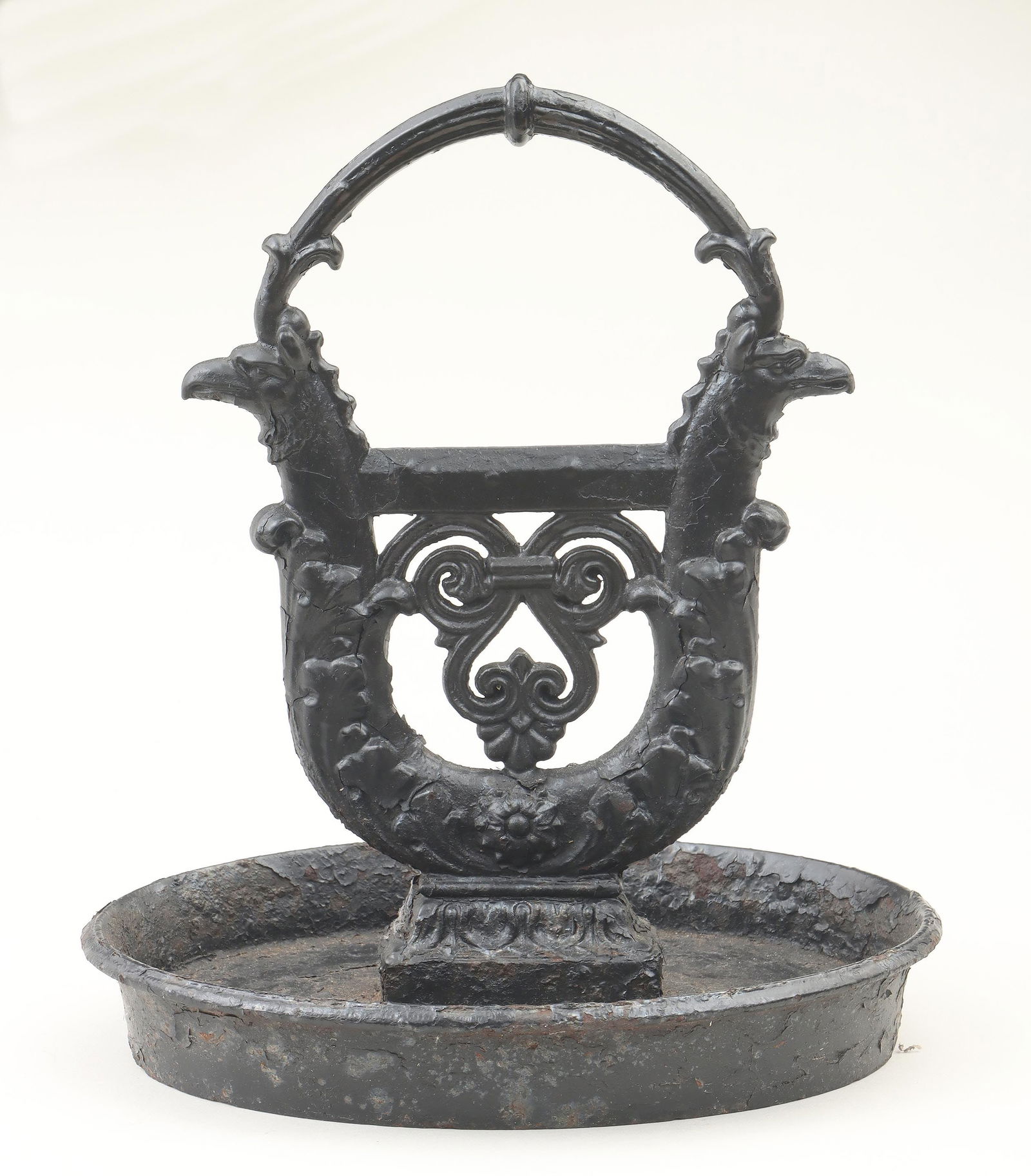 19th century English cast iron boot scrape: 19th century English black-painted cast iron boot scrape, having scrape of lyre form with griffin heads, scrolled foliate design and an arch over the top, in an oval tray. Wear, paint flaking, craquel