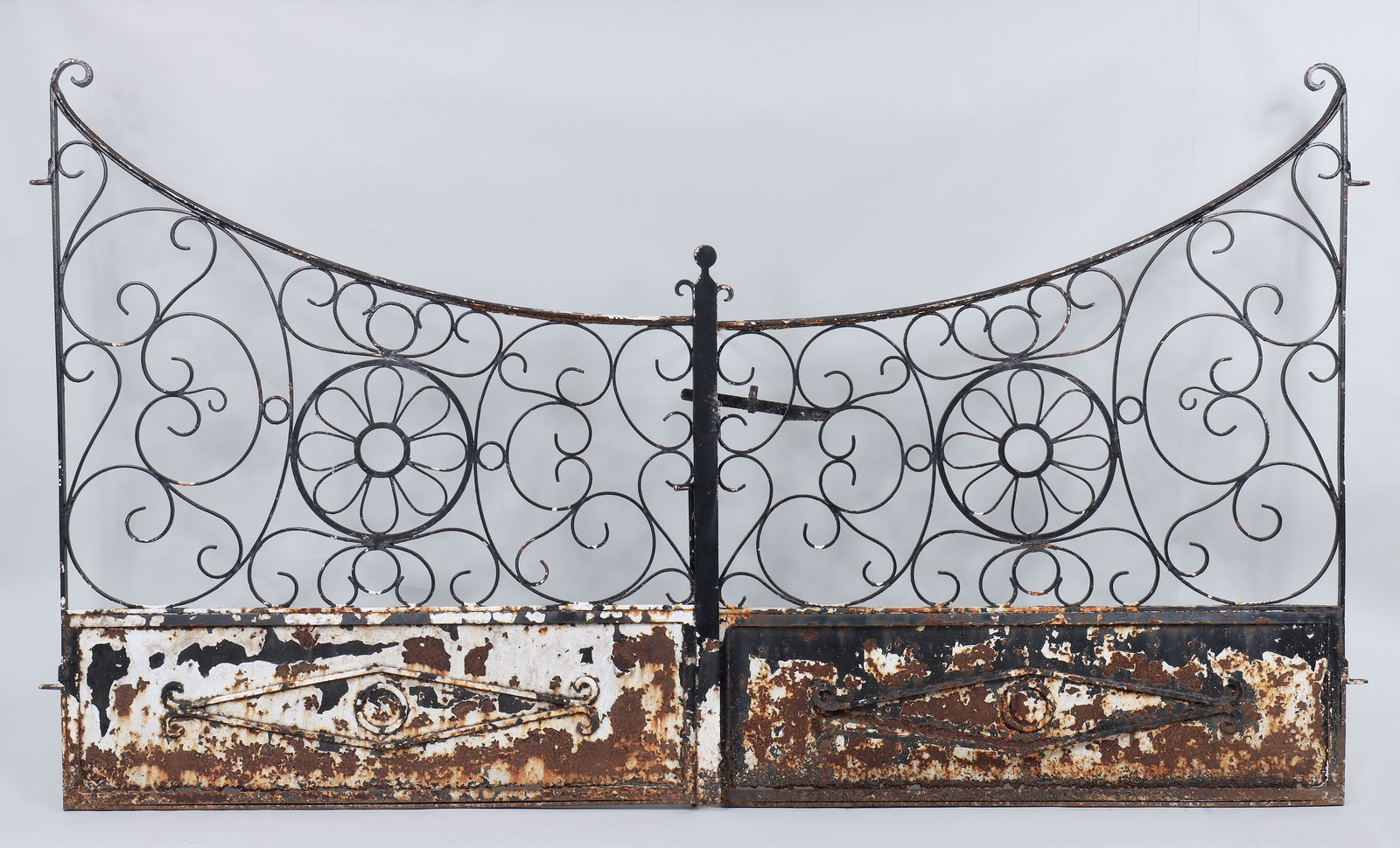 Pair of wrought iron gates: Pair of wrought iron gates with scrolled and floral designs. Paint loss, rust and losses to bottom, will need reconditioning. 63-1/2''h, 108''w.