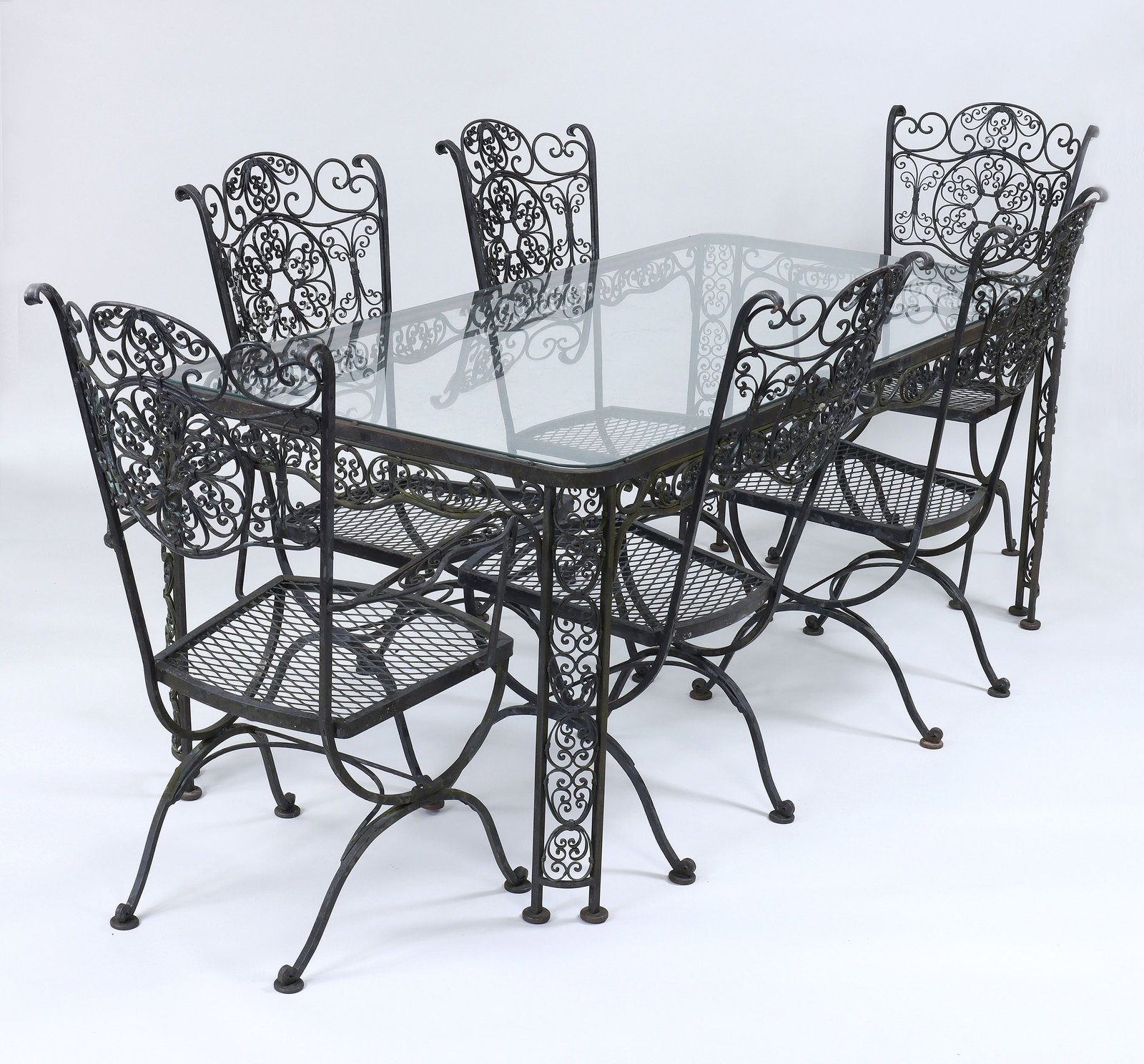 Russell Woodard seven-piece patio dining set: Russell Woodard seven-piece wrought iron patio dining set, decorated with scroll details in the Andalusian pattern, to include: glass-top rectangular table; (4) side chairs; and a pair of armchairs. W