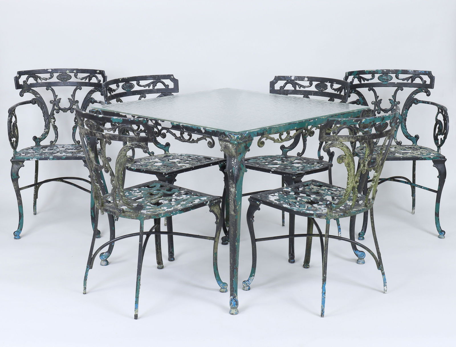 Seven-piece Florentine-style patio set: Seven-piece cast aluminum Florentine-style patio set, to include: pair of armchairs; (4) side chairs; and a square textured glass-top dining table. Paint loss, one armchair seat with hairline. Table 2
